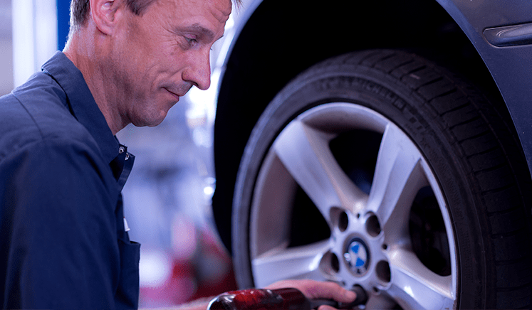 Smiling mechanic using a torque wrench to put lug nuts on a tire of a raised car