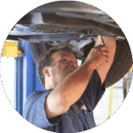 A Telle Tire technician working underneath a vehicle that is lifted high up on a lift in the garage.